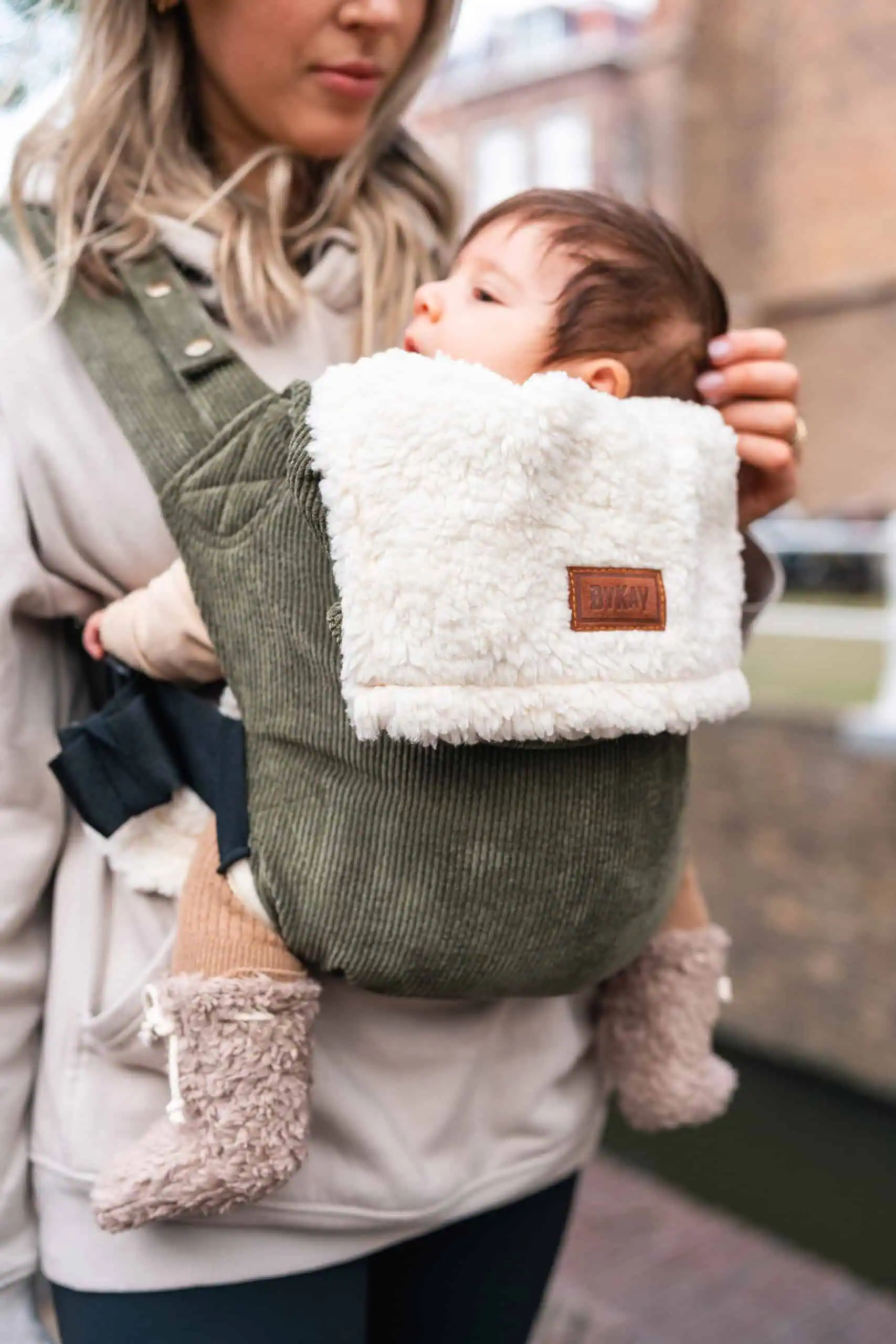 Baby carried close in an olive green carrier with a cream teddy inlay