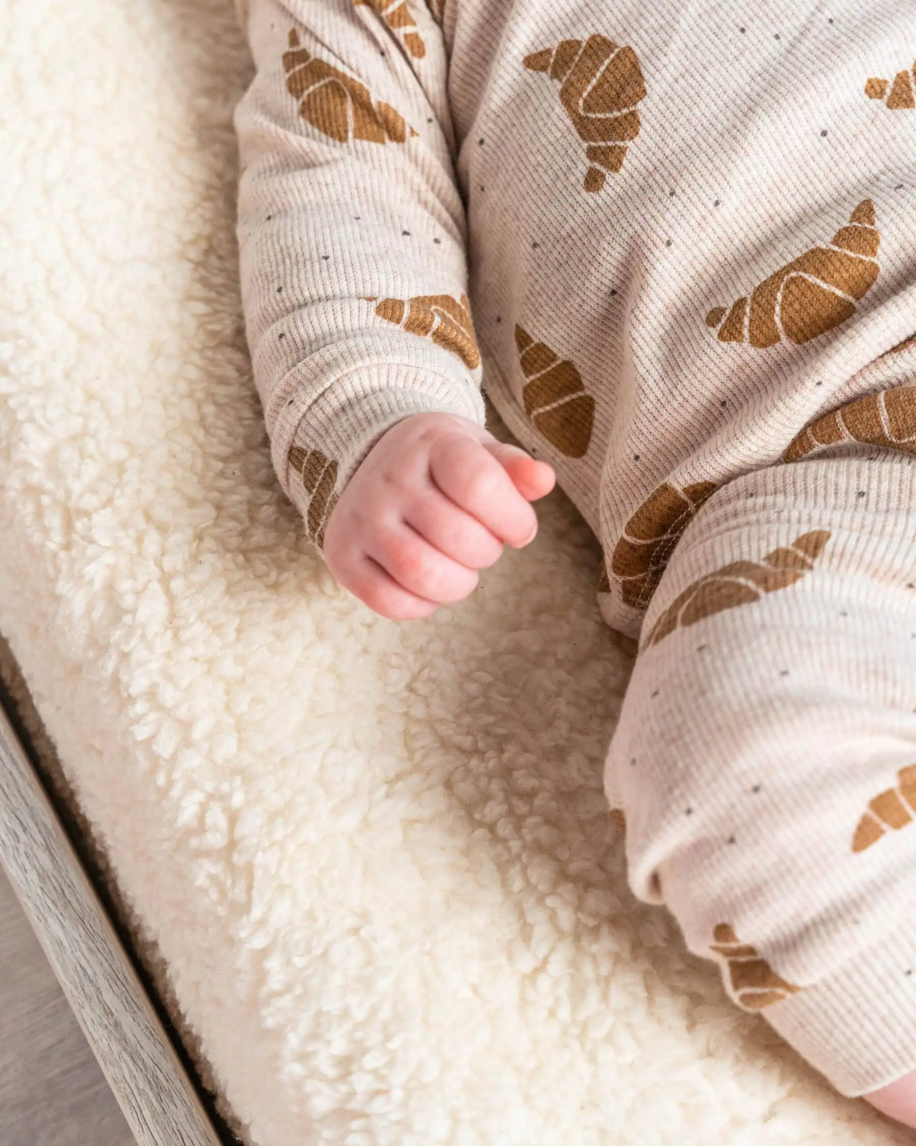 Baby hand clenched resting on a white fluffy sherpa blanket